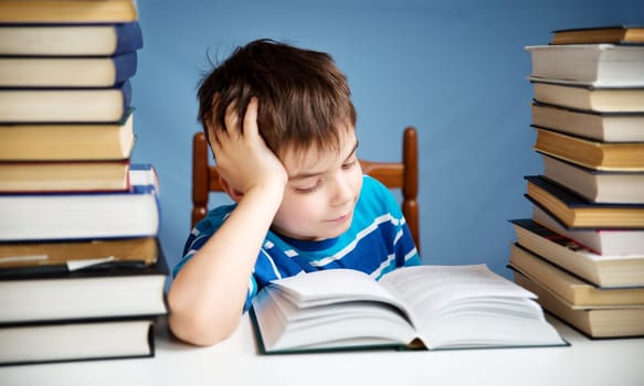 seven years old child reading a book at home. Boy studying at table on blue background