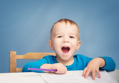 Little child drawing on the paper. Boy sitting on the chair at table with pencils