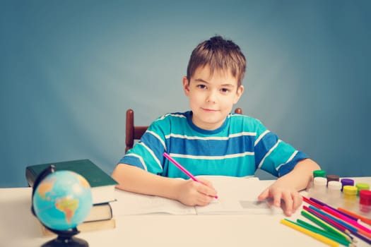 seven years old child writing at home. Boy studying at table on blue background. Kid drawing with a pencil