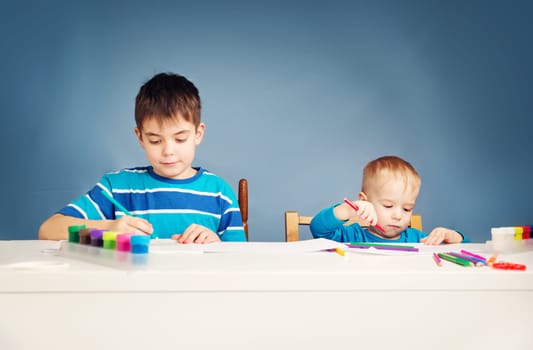 children writing at home. Boys studying at table on blue background. Kids drawing with pencils