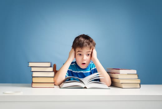 seven years old child reading a book at home. Boy studing at table on blue background
