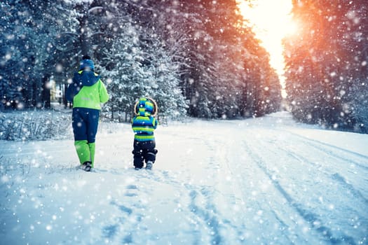 Children walking on snow at snowfall. Boys in winter clothes outdoors in cold weather
