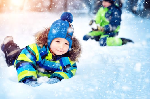 Children playing in snow at snowfall. Boys in winter clothes outdoors in cold weather