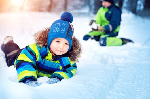 Children playing in snow at snowfall. Boys in winter clothes outdoors in cold weather