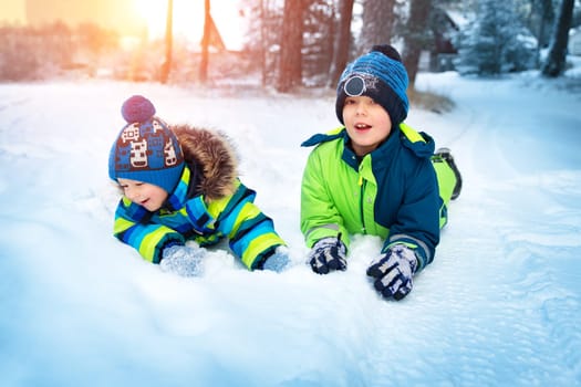 Children playing in snow at snowfall. Boys in winter clothes outdoors in cold weather