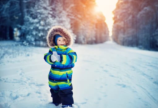 Baby boy walking at snowfall. Child in winter clothes playing with snow