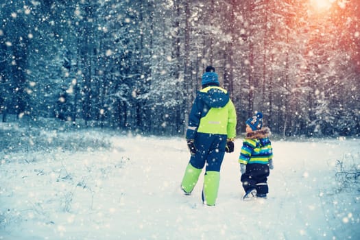Children playing in snow at snowfall. Boys in winter clothes outdoors in cold weather