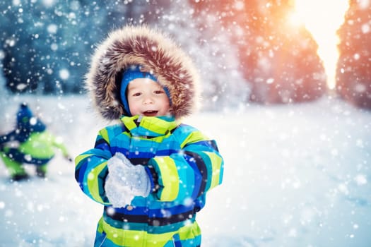 Baby boy walking at snowfall. Child in winter clothes playing with snow