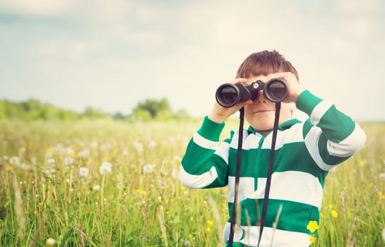 Child wathing in benoculars on the field with dandelions. Boy playing on the meadow in summer