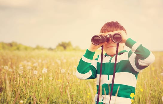 Child wathing in benoculars on the field with dandelions. Boy playing on the meadow in summer