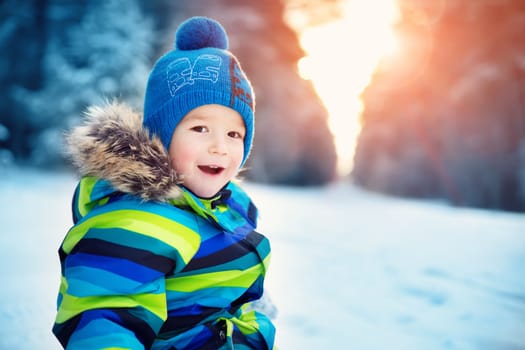 Baby boy walking at snowfall. Child in winter clothes playing with snow