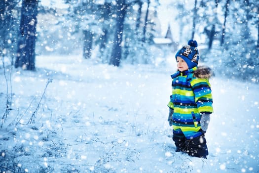 Baby boy smiling at snowfall. Child in winter clothes