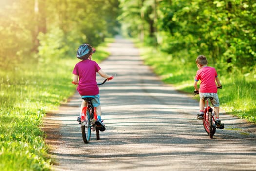 children riding on a bicycles at asphalt road in the park in summer