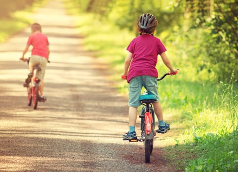children riding on a bicycles at asphalt road in the park in summer