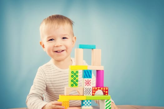 Portrait of a two years old child stacking wooden cubes. Pretty little boy on blue background