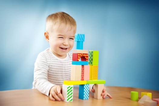 Portrait of a two years old child stacking wooden cubes. Pretty little boy on blue background