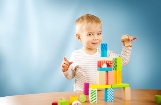 Portrait of a two years old child stacking wooden cubes. Pretty little boy on blue background