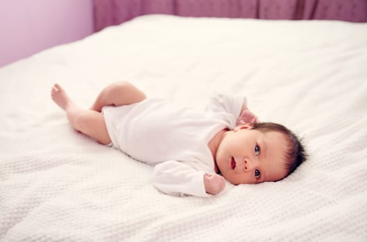 Cute newborn baby girl lying in the bed. Two weeks old infant child on white soft blanket