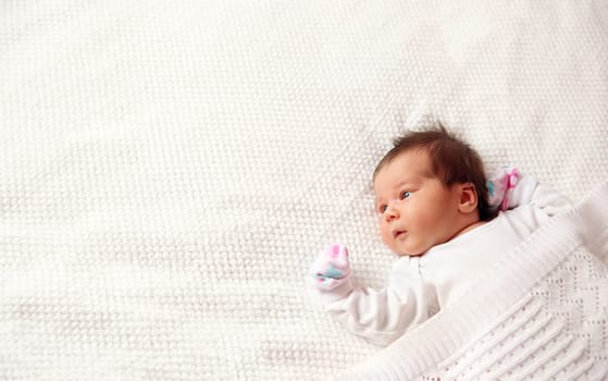 Cute newborn baby girl lying in the bed. Two weeks old infant child on white soft blanket