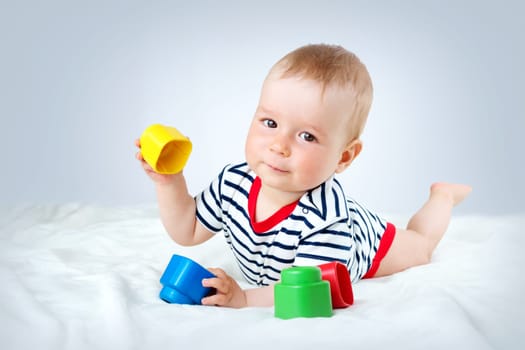 Nine month old baby lying in the bed on white blanket. Cute boy playing with cubes