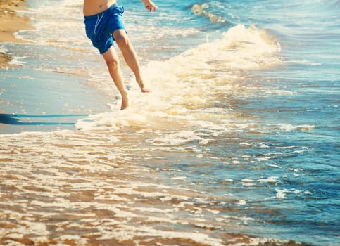 boy barefoot is jumping on the beach in water. Child is on vacation in summer at the sea