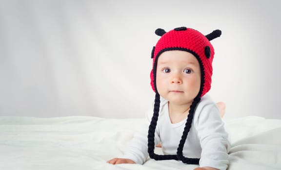 Cute baby lying in the bed on white blanket in knitted ladybug hat. Pretty little boy