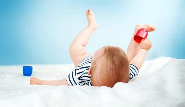Nine month old baby lying in the bed on white blanket. Cute boy playing with cubes