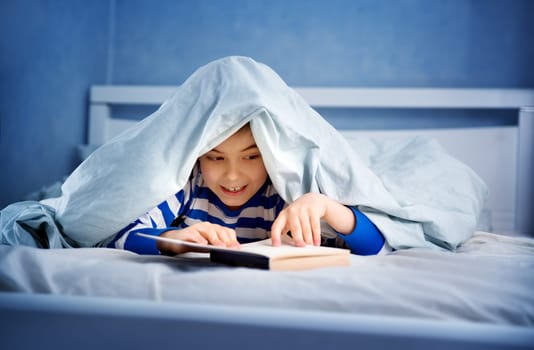 boy lying in bed with a book. child reading