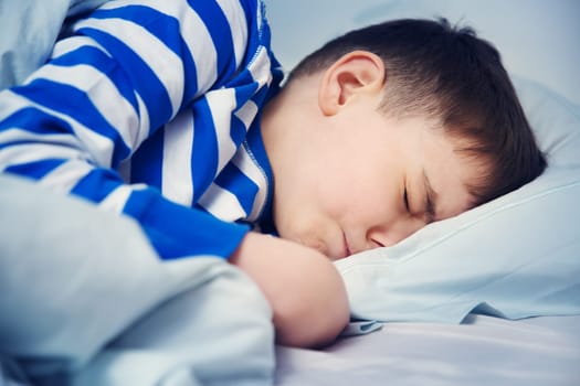 Boy sleeping in bed in pajamas. Child lying in bed on pillow at night
