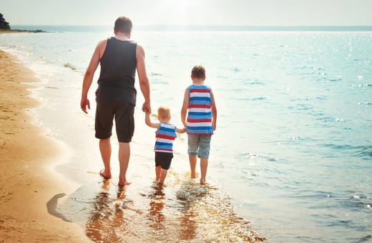 Father and sons walking at the beach at sea. A man with children resting at seaside in summer on sunny day