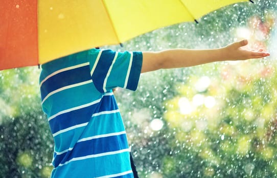 Child on rainy weather. Boy holding colourful umbrella under rain in summer