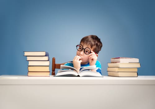 seven years old child reading a book at home. Boy studing at table on blue background