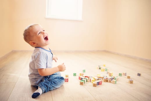 two years old child sitting on the floor. Pretty little boy palying with wooden cubes at home