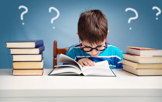 seven years old child reading a book at home. Boy studing at table on blue background