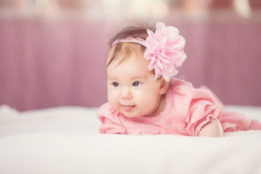 Cute little baby girl lying in the bed in pink dress. Three month old infant child on white soft blanket