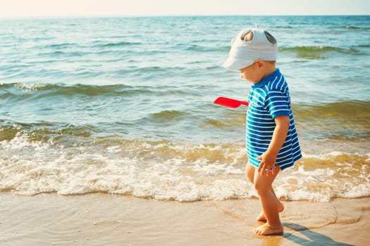 one year old boy walking at the beach in summer hat. Child on family vacations at sea