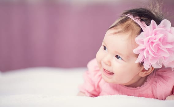 Cute little baby girl lying in the bed in pink dress. Three month old infant child on white soft blanket