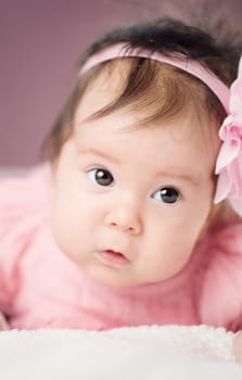 Cute little baby girl lying in the bed in pink dress. Three month old infant child on white soft blanket