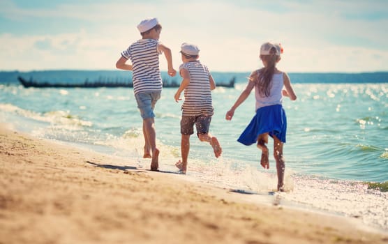 children jumping on the beach in summer hats. Boys and girl having fun at seaside