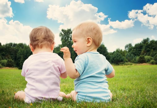 Babygirl and babyboy sitting in the grass on sunny day
