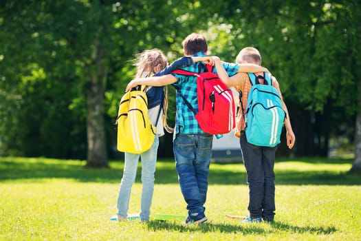 Children with rucksacks standing in the park near school. Pupils with books and backpacks outdoors
