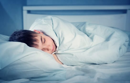 Boy sleeping in bed in pajamas. Child lying in bed on pillow at night