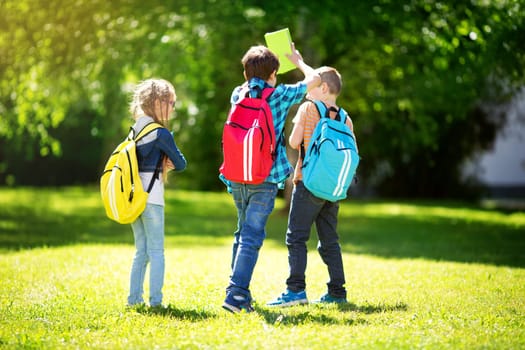 Children with rucksacks standing in the park near school. Pupils with books and backpacks outdoors