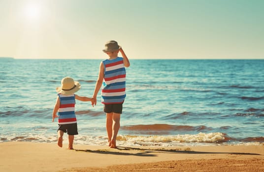 Two brothers barefoot are walking on the beach in water. Boys are on vacation in summer at the sea