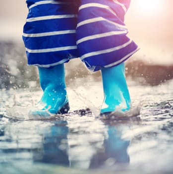 Child walking in wellies in puddle on rainy weather. Boy under rain in summer