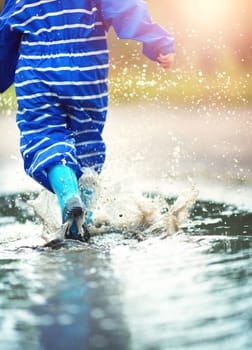 Child walking in wellies in puddle on rainy weather. Boy under rain in summer