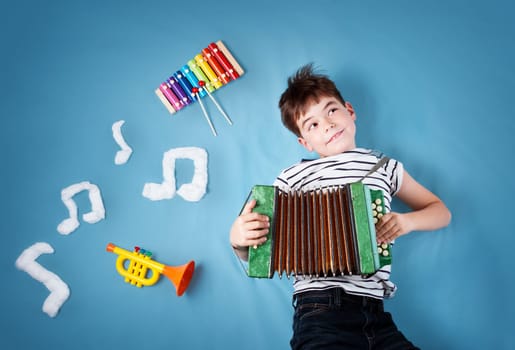 happy seven years old boy on blue blanket background with accordion and musical notes. Young child singing song