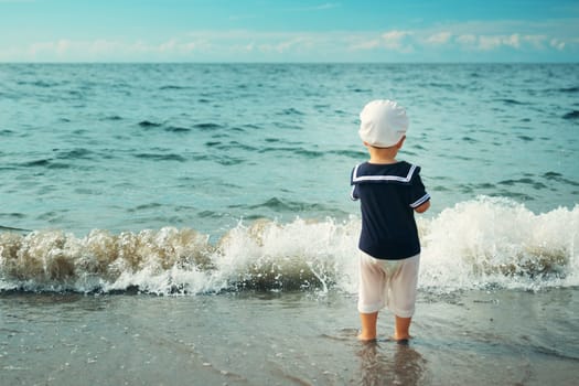 one year old boy walking at the beach in straw hat. Child on family vacations at sea