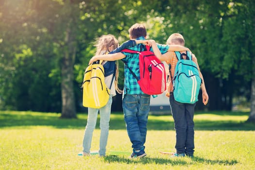 Children with rucksacks standing in the park near school. Pupils with books and backpacks outdoors