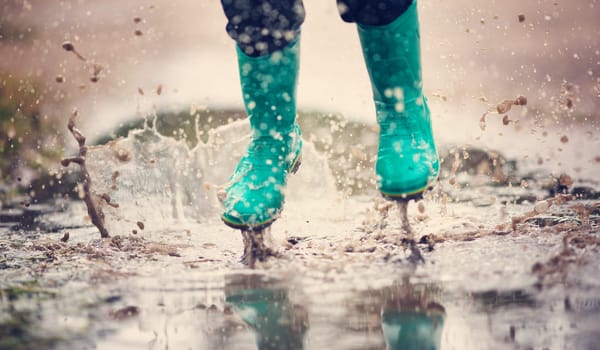 Child walking in wellies in puddle on rainy weather. Boy under rain in summer